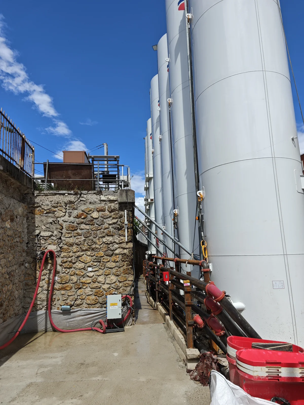 Rangée de grands silos blancs et tuyauteries de distribution sur une centrale.